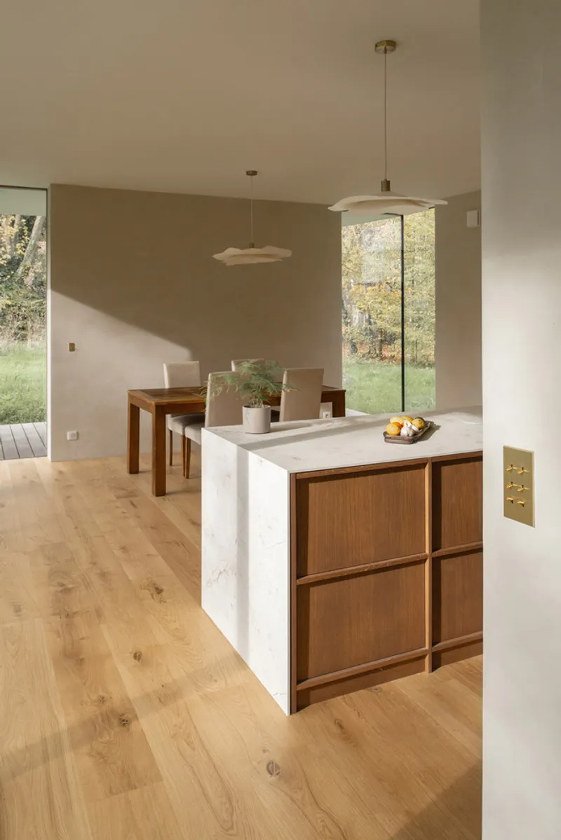 Kitchen island with walnut cabinet base and stone countertop beside dining area with pendant lighting
