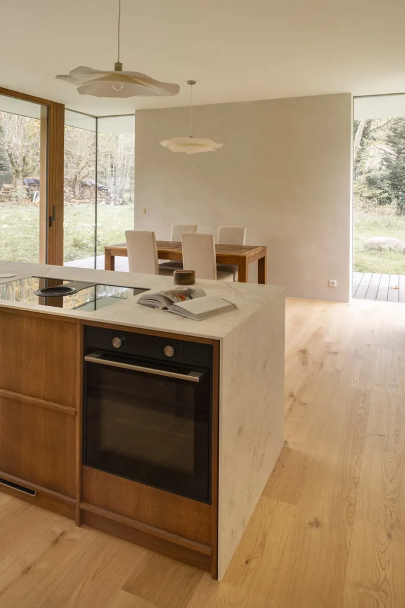 Open kitchen and dining space with stone island and timber table beneath layered paper pendant lights