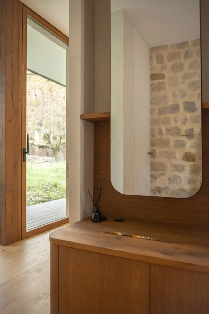 Bathroom vanity with timber cabinetry and rounded mirror reflecting exposed stone wall behind
