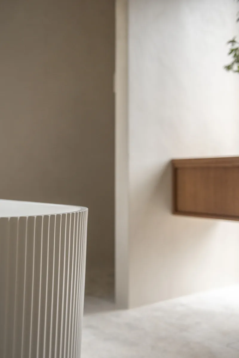 Close-up of white fluted bathtub edge against soft grey plastered walls