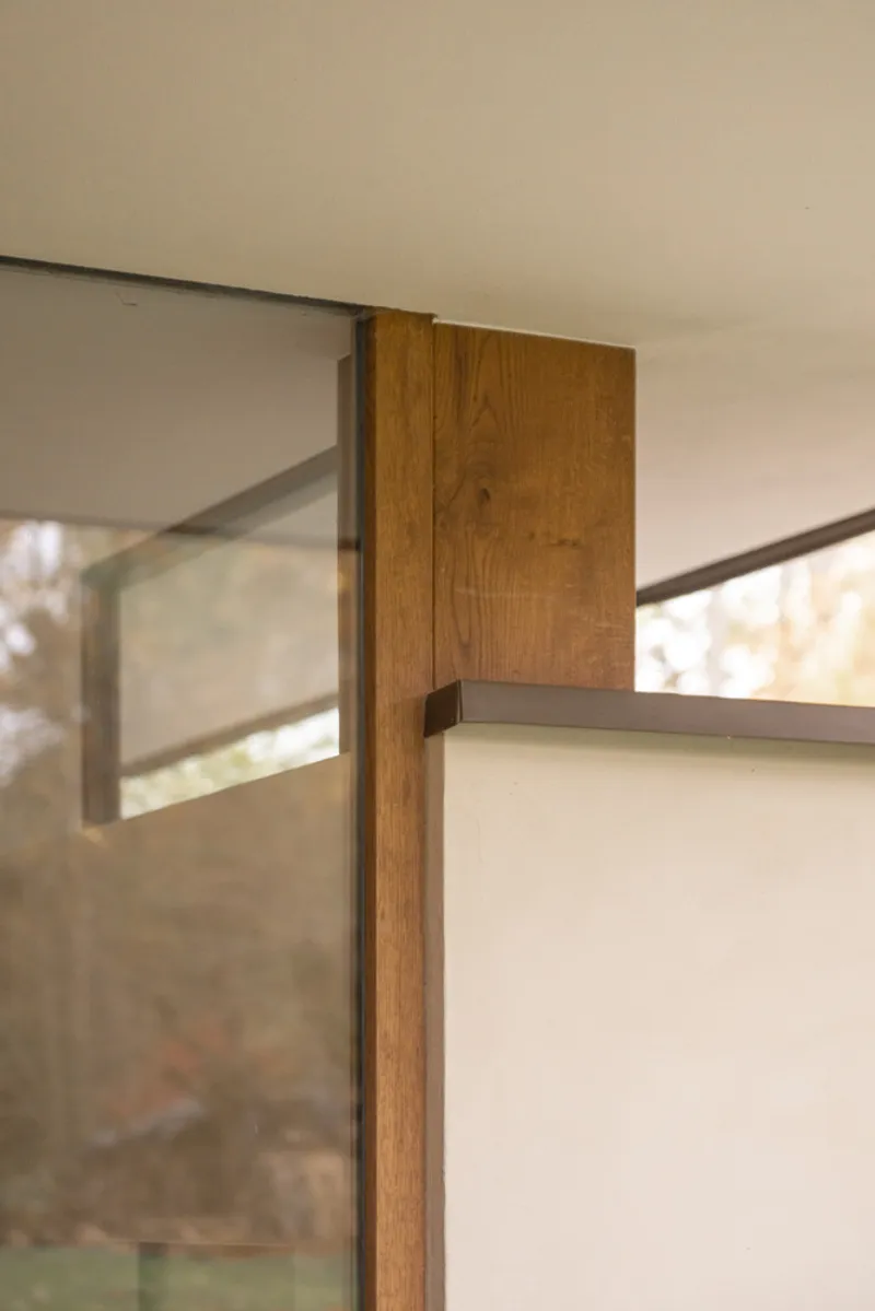 Junction of oak post with glazing frame and pale plastered wall at ceiling