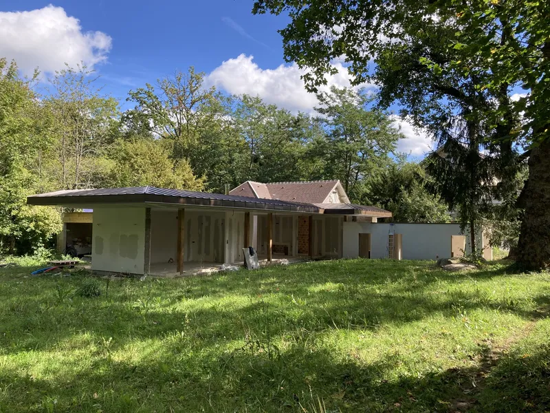 Side view of the single-story addition with covered terrace beneath trees on a sunny afternoon