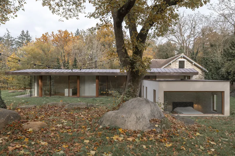 Garden facade with metal standing-seam roof and large boulder beneath a canopy of autumn trees