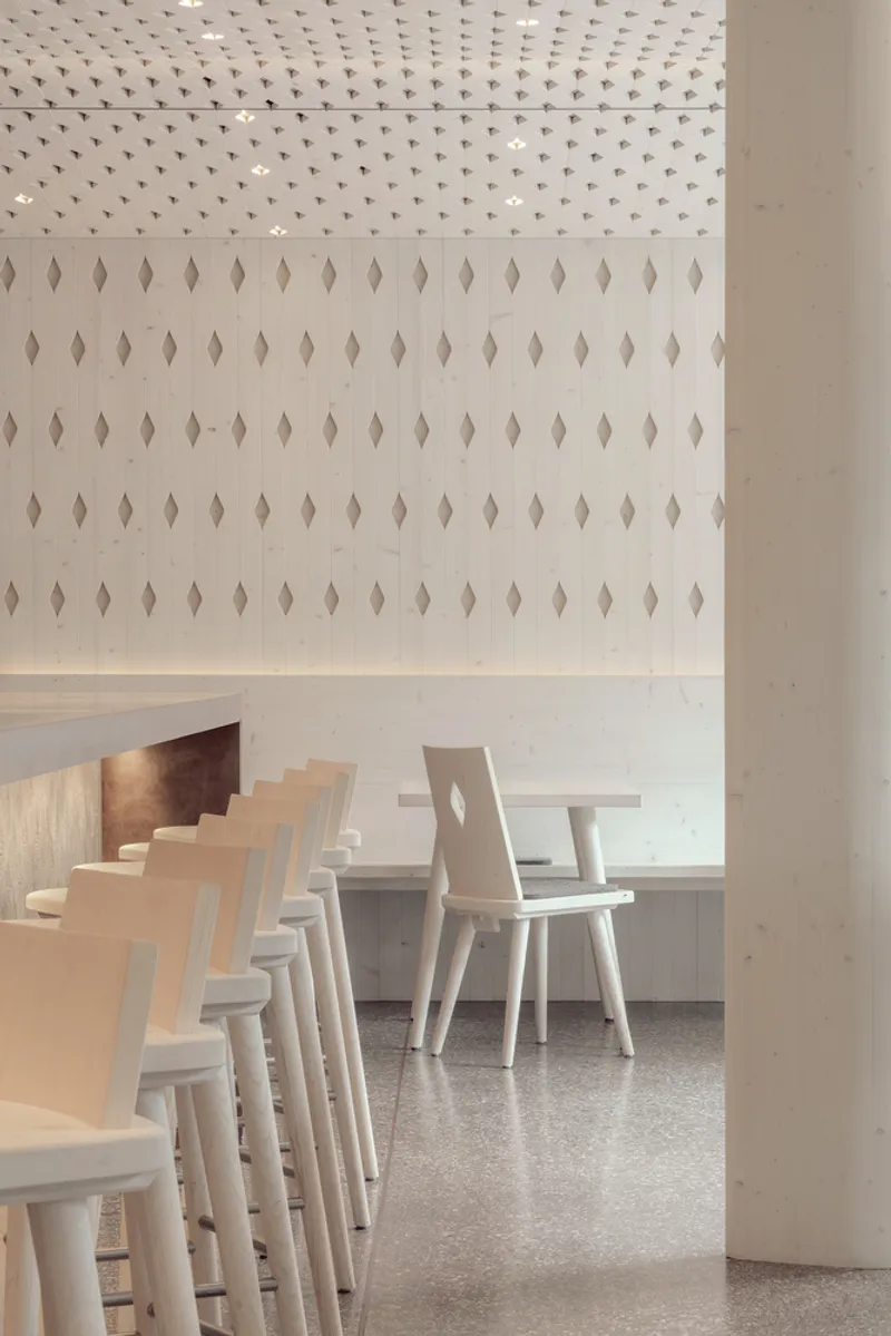 Light wood dining chairs lined along a wall with diamond-shaped apertures in vertical pattern