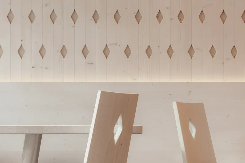 Close-up of two chairs with teardrop cutouts against pale timber paneling and table edge