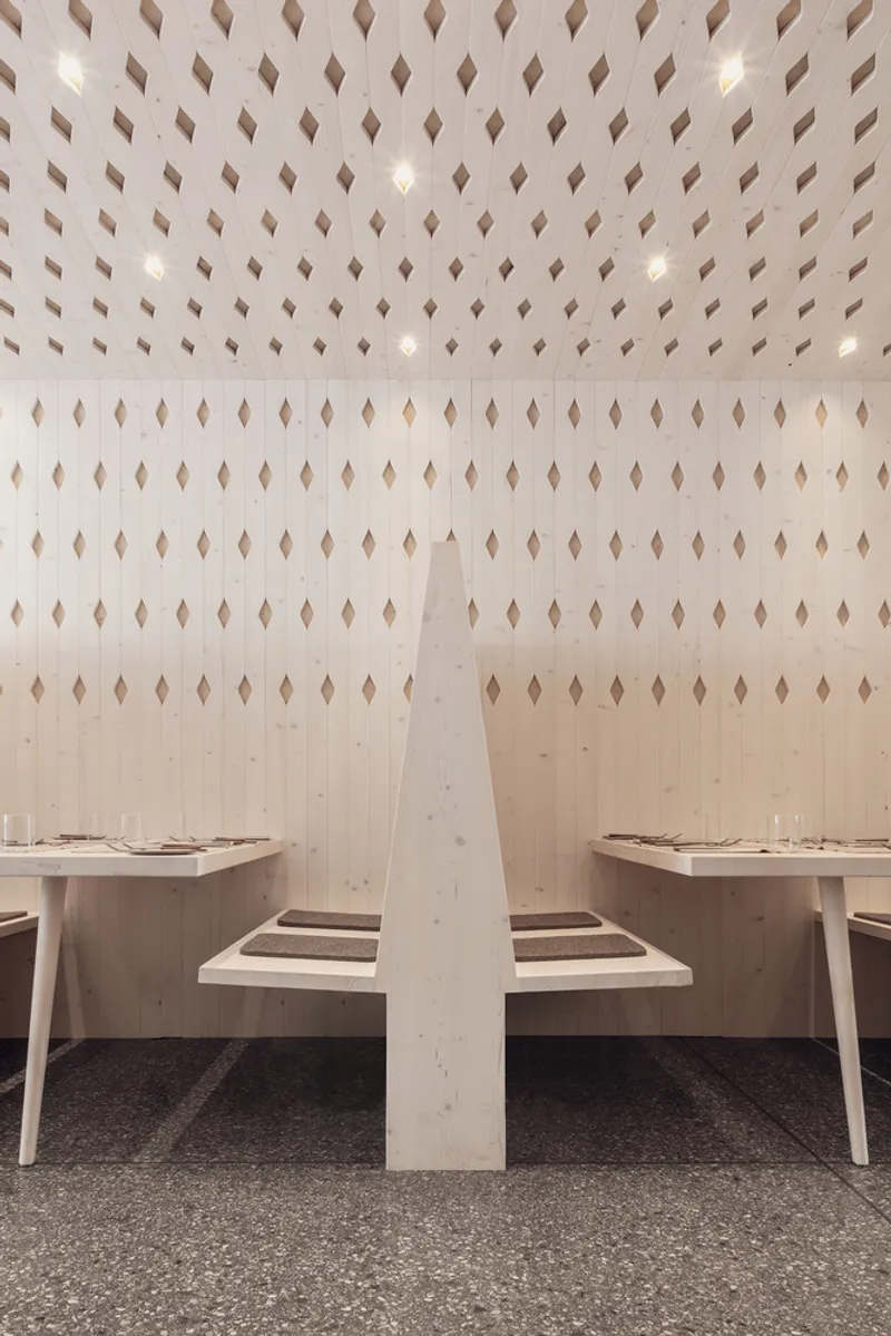 Dining booth with central timber partition flanked by seating under a perforated ceiling