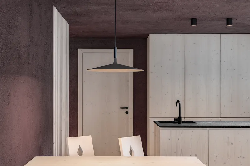 Dining area with light wood table, black pendant fixture, and textured concrete walls
