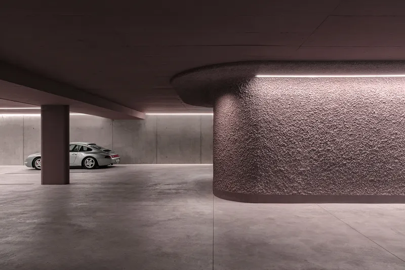 Underground parking garage with textured wall panel, cylindrical column, and recessed strip lighting overhead