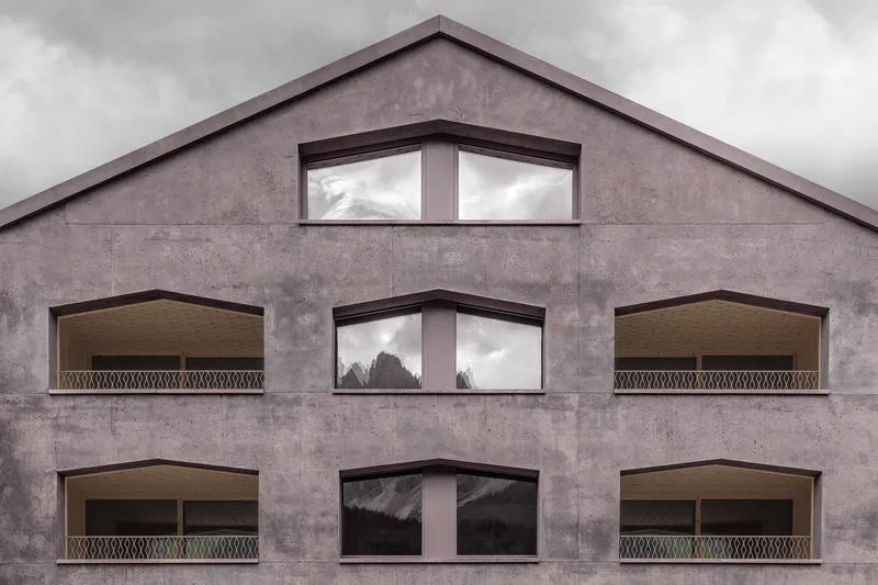 Facade with corner windows and recessed balconies featuring perforated metal railings on a gabled concrete wall