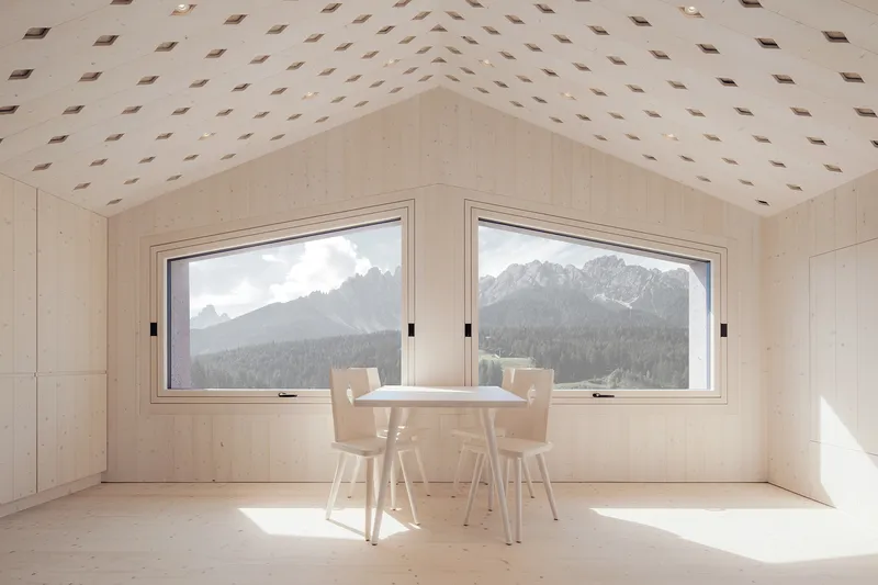 Interior dining space with light wood table and chairs beneath diamond-patterned ceiling openings framing mountain views