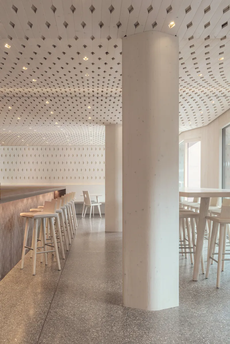 Dining hall with circular concrete column and perforated timber ceiling over terrazzo flooring and bar seating