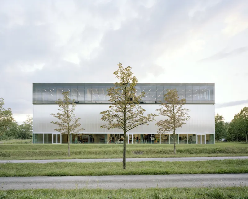 Street facade with translucent upper volume cantilevered over glazed ground floor and three planted trees