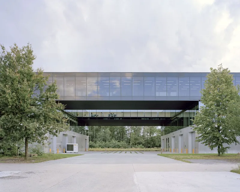 Entry drive passing beneath the elevated bridge with flanking security kiosks and mature trees