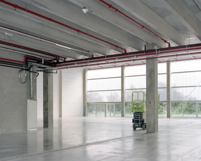Open interior with polished concrete floor, exposed red mechanical piping, and translucent window blinds