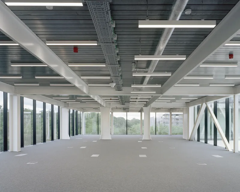 Open interior floor with exposed white structural beams and corrugated metal ceiling under linear lighting
