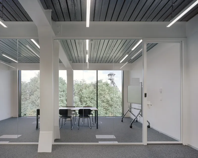 Glass-walled meeting room with table and chairs overlooking trees through floor-to-ceiling windows