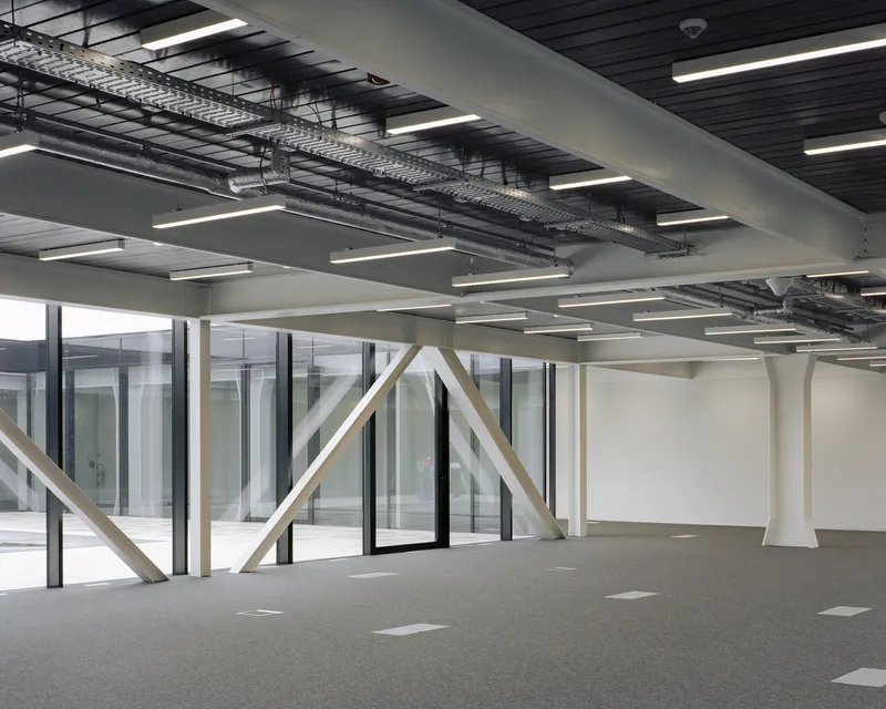 Interior corner showing white diagonal bracing against glazed curtain wall and exposed cable trays overhead