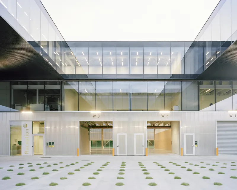 Courtyard elevation showing three loading bays, glazed skybridge, and grass-grid paving with uniform planting