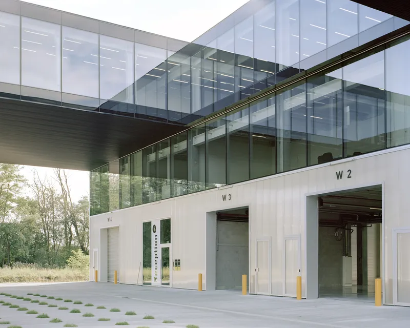 Loading dock entries beneath cantilevered glass bridge with corrugated metal doors and yellow bollards