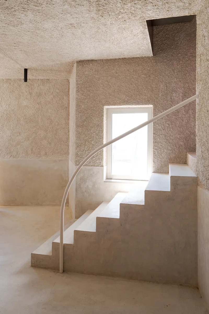 Stairwell with curved steel handrail and textured plaster walls framing a deep window opening