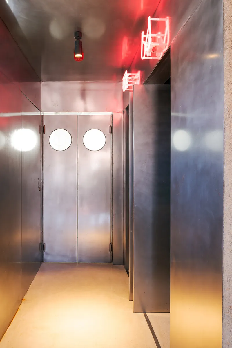 Stainless steel corridor with circular portal doors and red neon signage overhead