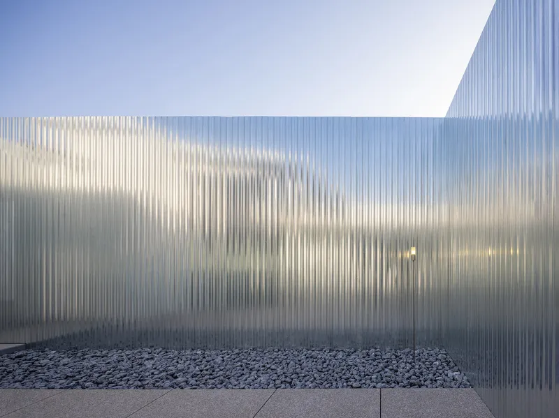 Angled view of translucent corrugated polycarbonate walls meeting at a corner above a gravel bed