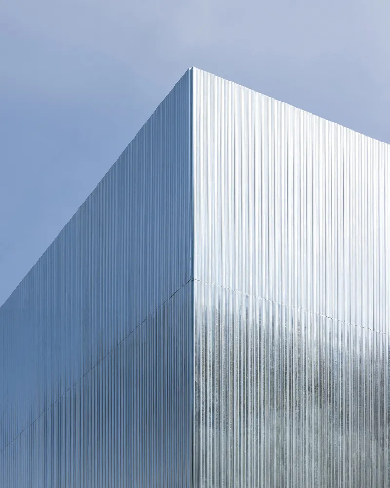 Vertical corrugated metal facade catching bright sunlight against a clear blue sky