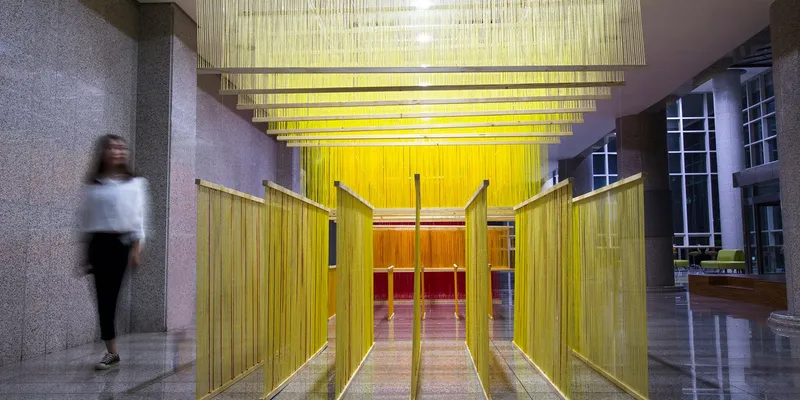 Entry passage through the yellow string installation with a blurred figure walking in the lobby at dusk