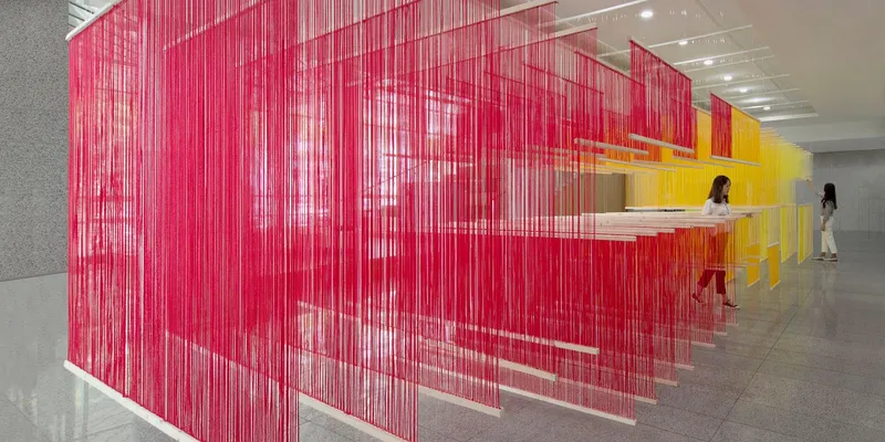 Layered suspended panels of pink and yellow thread creating translucent partitions in a lobby
