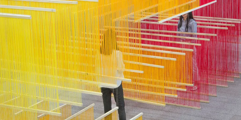Close view through overlapping colored thread panels with a visitor visible between the layers