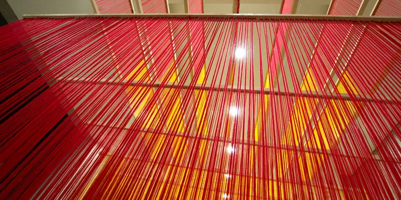 Upward view through layers of pink and orange thread with recessed ceiling lights visible above