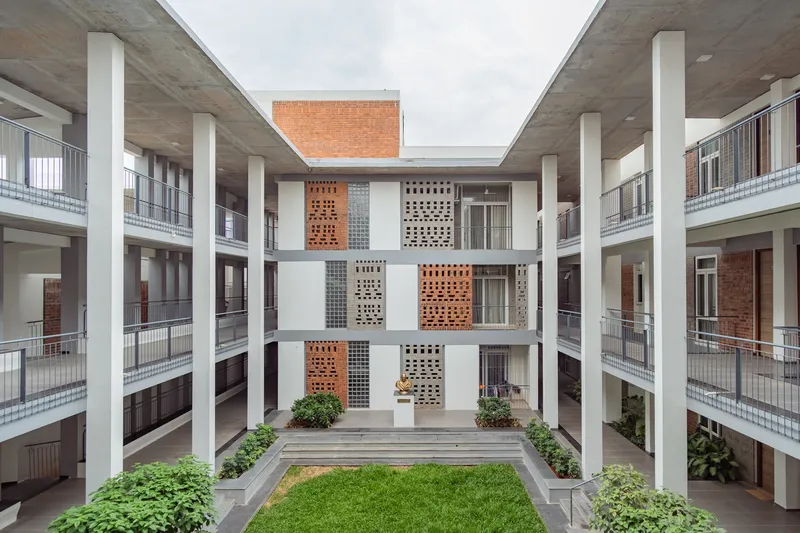 Central courtyard with grass lawn and planted beds framed by concrete columns and perforated brick screens