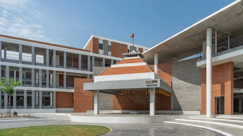 Entry pavilion with terracotta tile roof and white columns set in a paved forecourt under blue sky