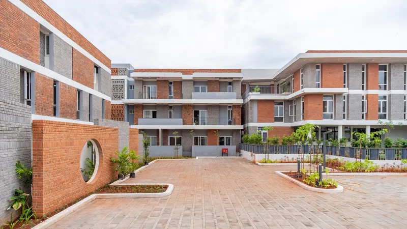 Paved courtyard with planted beds and circular window in terracotta brick wall under cloudy sky