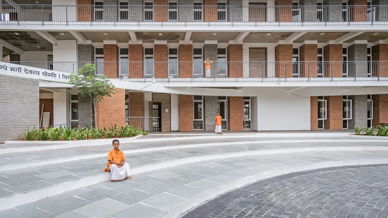 Facade with alternating red and grey brick panels framing doorways as person sits in courtyard