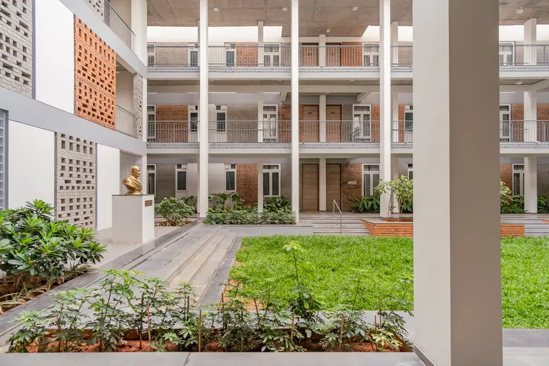 Interior courtyard with grass lawn, planted beds and white columns framing residential balconies beyond