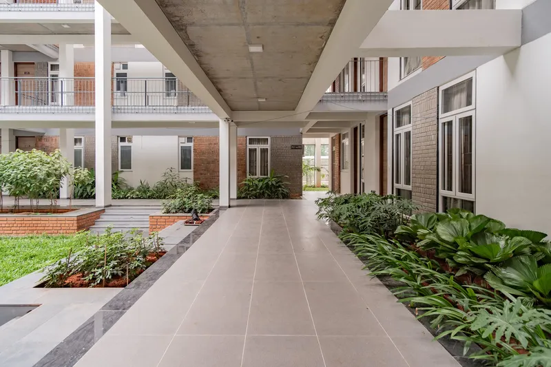 Covered walkway with exposed concrete soffit and steel columns overlooking planted beds and residential units