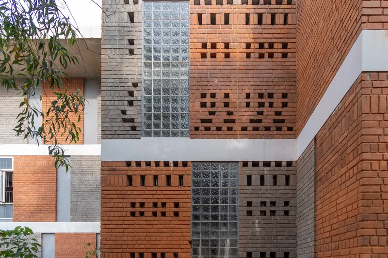 Facade composition of red and grey perforated brick panels with vertical glass block strip and white beam