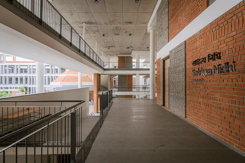 Upper level corridor with black metal railing overlooking open atrium space and textured brick wall with signage