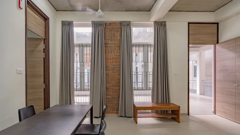 Interior room with exposed brick column framed by tall windows with grey curtains and concrete ceiling