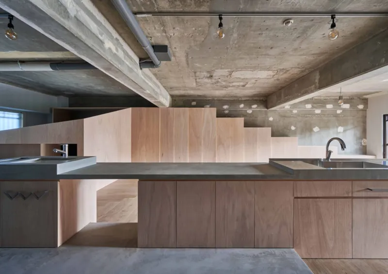 Kitchen island with timber cabinetry and dark countertop beneath exposed concrete ceiling with track lighting
