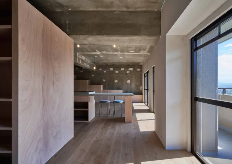 Kitchen island with timber table and stools beneath an exposed concrete ceiling with recessed lighting