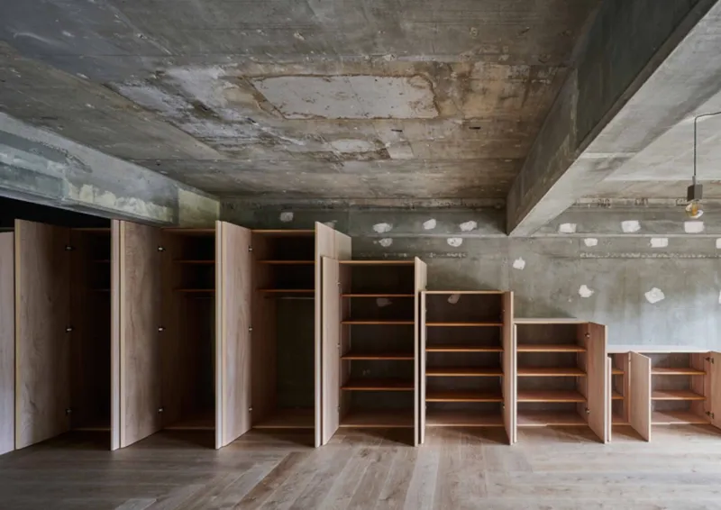 Stepped storage wall with open doors revealing shelving under weathered concrete ceiling