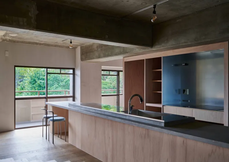 Open kitchen with light wood cabinetry and exposed concrete ceiling beams overlooking a green balcony