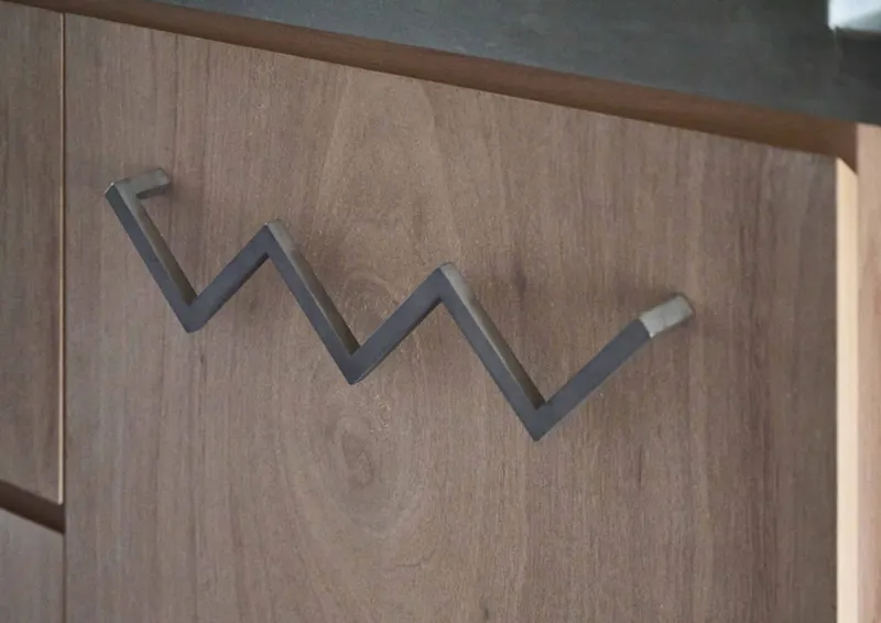 Close-up of a zigzag steel coat hook mounted on a light wood cabinet door