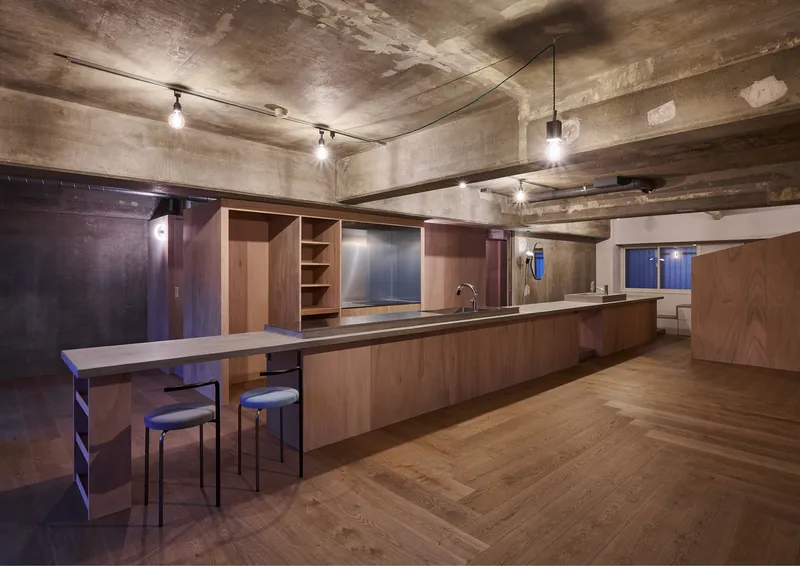 Kitchen with timber cabinetry and breakfast bar beneath exposed concrete beams and track lighting at night