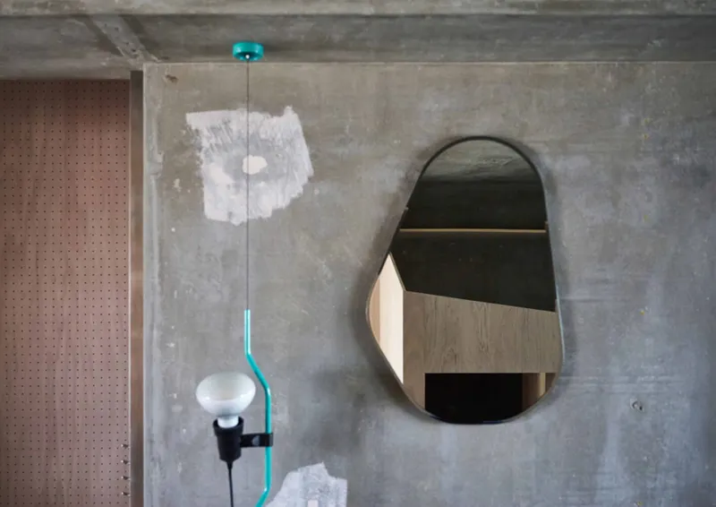 Oval mirror and pendant light with turquoise cord against patched concrete wall