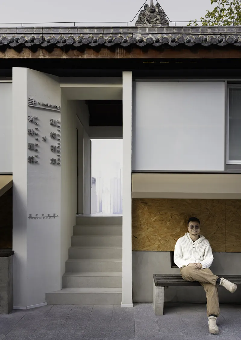 Concrete stairs leading to a narrow doorway beneath the traditional tiled roof eave with a seated figure