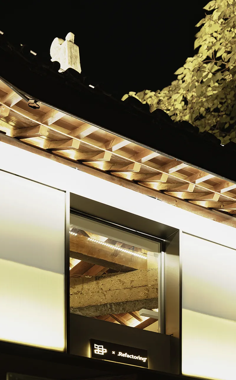 Underlit timber eave with geometric bracket pattern above a backlit entrance at night