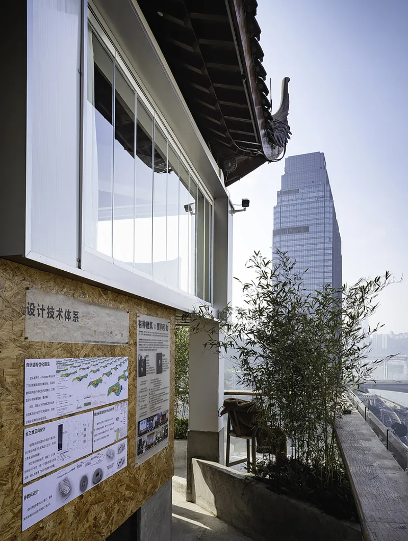 Exterior terrace with plywood signage, planted bamboo in concrete planters, and a highrise tower beyond